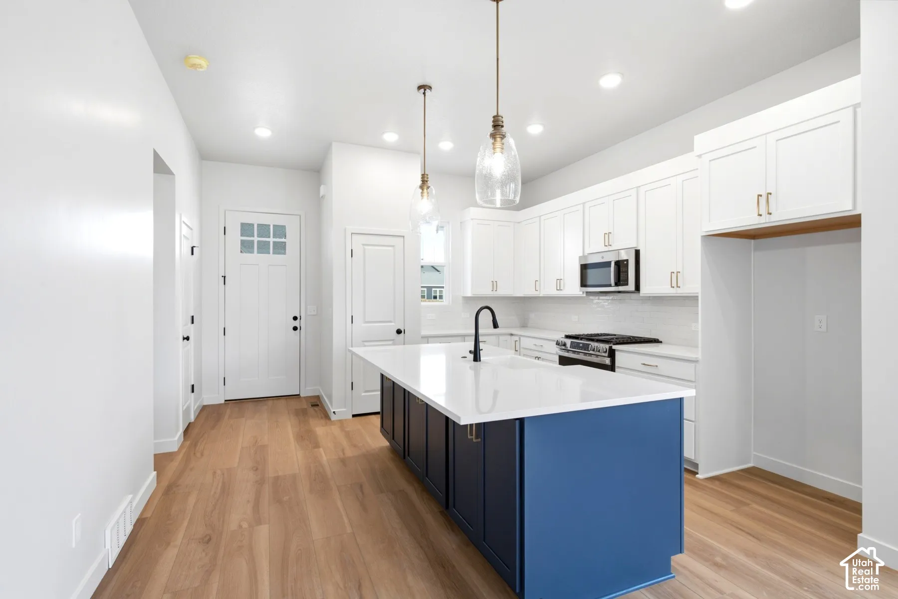Open-concept kitchen featuring a large central island with a contrasting finish, white shaker cabinetry, stainless steel appliances, and wood-finish flooring