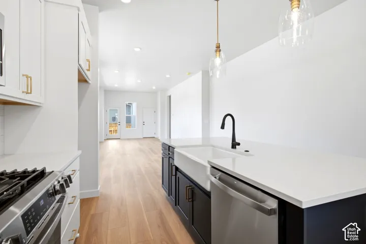 White cabinetry with gold-tone hardware, stainless steel gas range, white countertops, farmhouse sink with matte black faucet, and wood-finish flooring