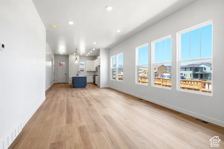 Open-concept layout with wood-finish flooring, recessed lighting, multiple windows, and a kitchen featuring an island with a sink and pendant lighting