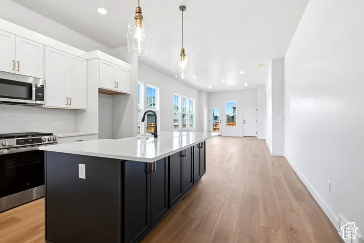Modern kitchen featuring a large island with white countertops, stainless steel appliances, and wood-finish flooring