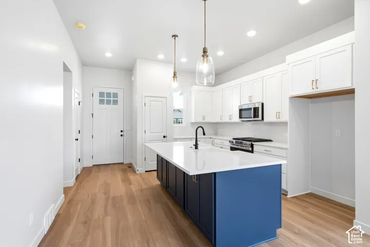 Open-concept kitchen featuring a large central island with a contrasting finish, white shaker cabinetry, stainless steel appliances, and wood-finish flooring