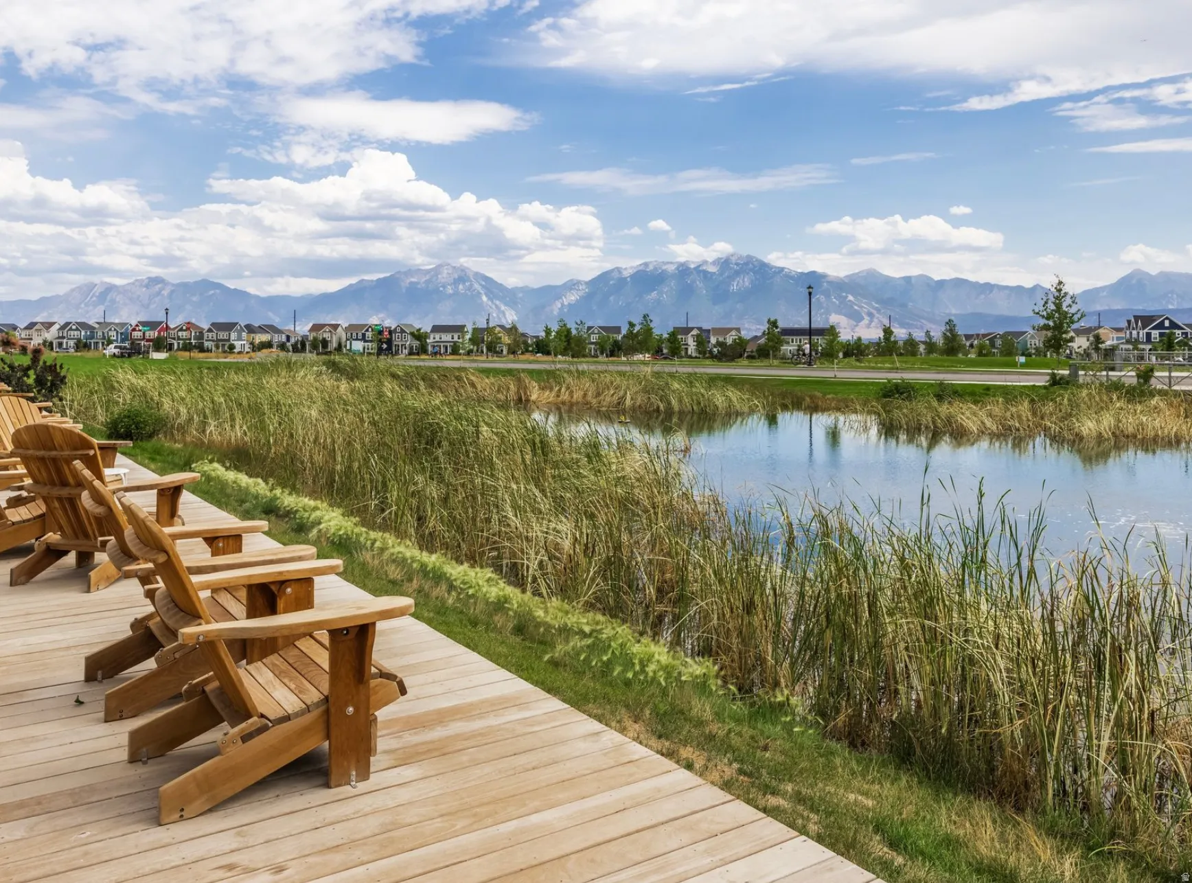 Expansive outdoor wood deck with a natural water feature, surrounding green landscaping, and distant mountains