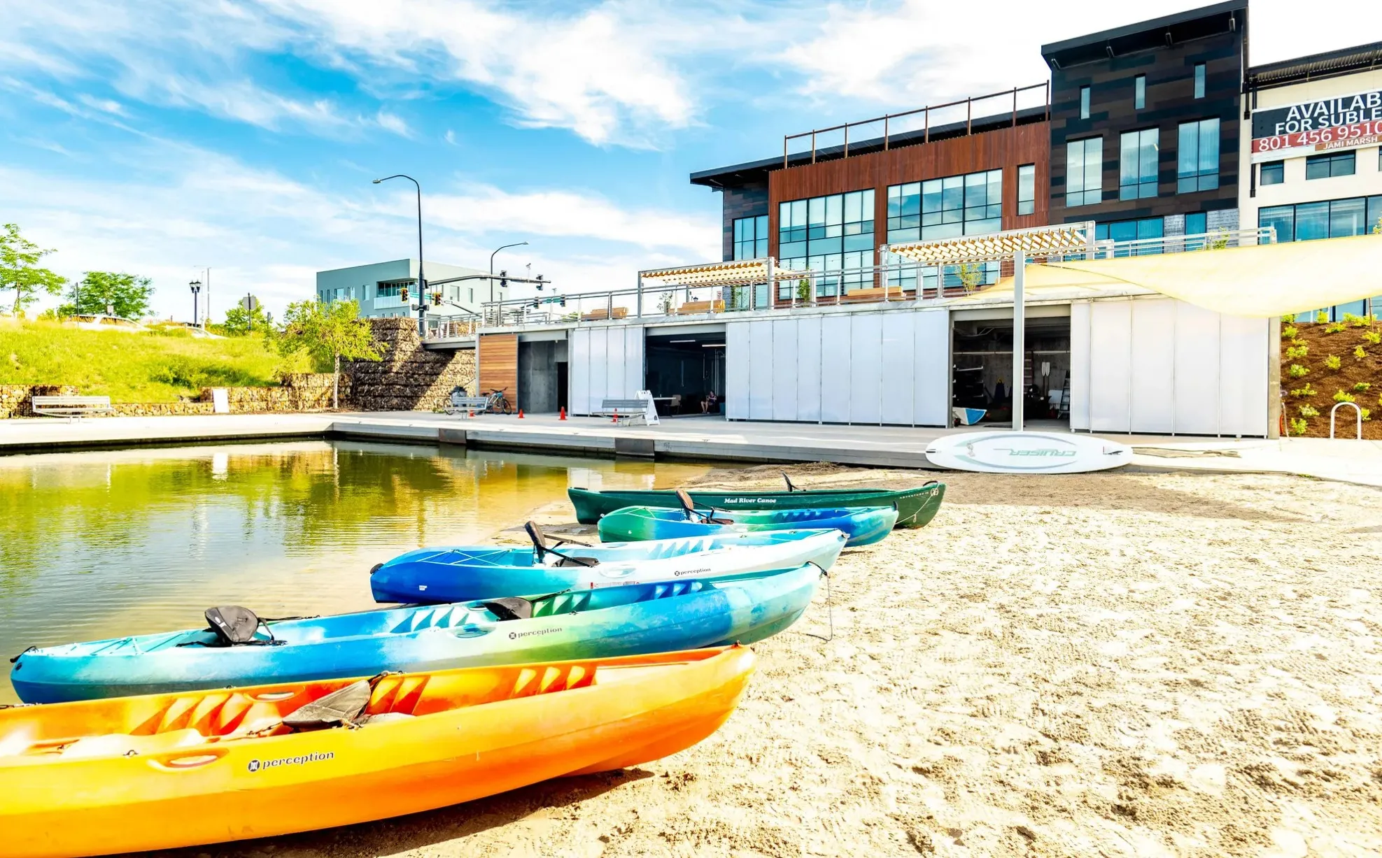 Waterfront property featuring a sandy beach area, multi-story building with large windows, and a shaded outdoor structure