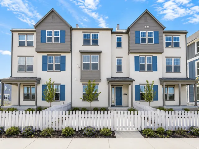 Contemporary townhome exterior featuring stucco siding, gabled roof accents, blue window shutters, and a white picket fence