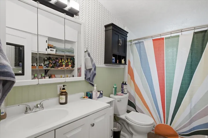 White vanity with integrated sink, chrome faucet, medicine cabinet with mirrored doors, wall-mounted storage cabinet, and beadboard wainscoting