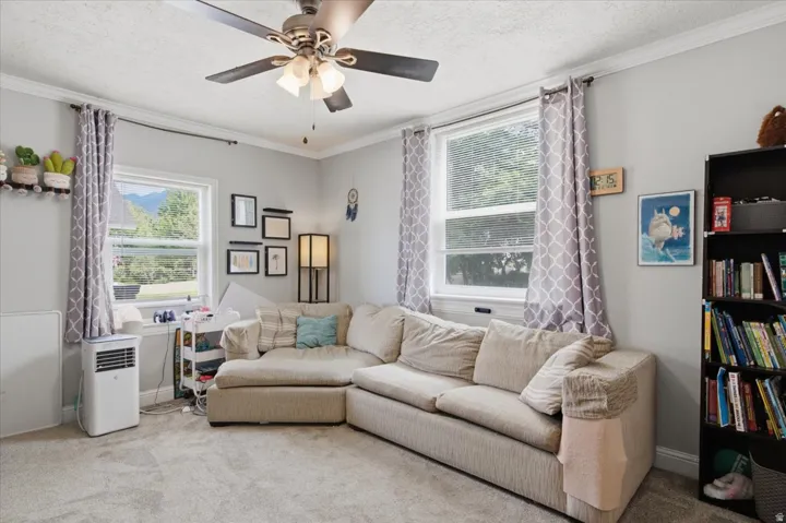Carpeted room featuring a ceiling fan with integrated lighting, crown molding, and multiple windows