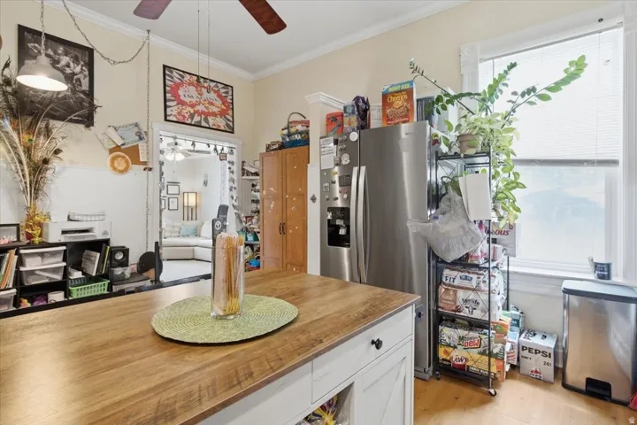 Kitchen featuring a wood-finish island, stainless steel refrigerator, wood-finish flooring, and crown molding