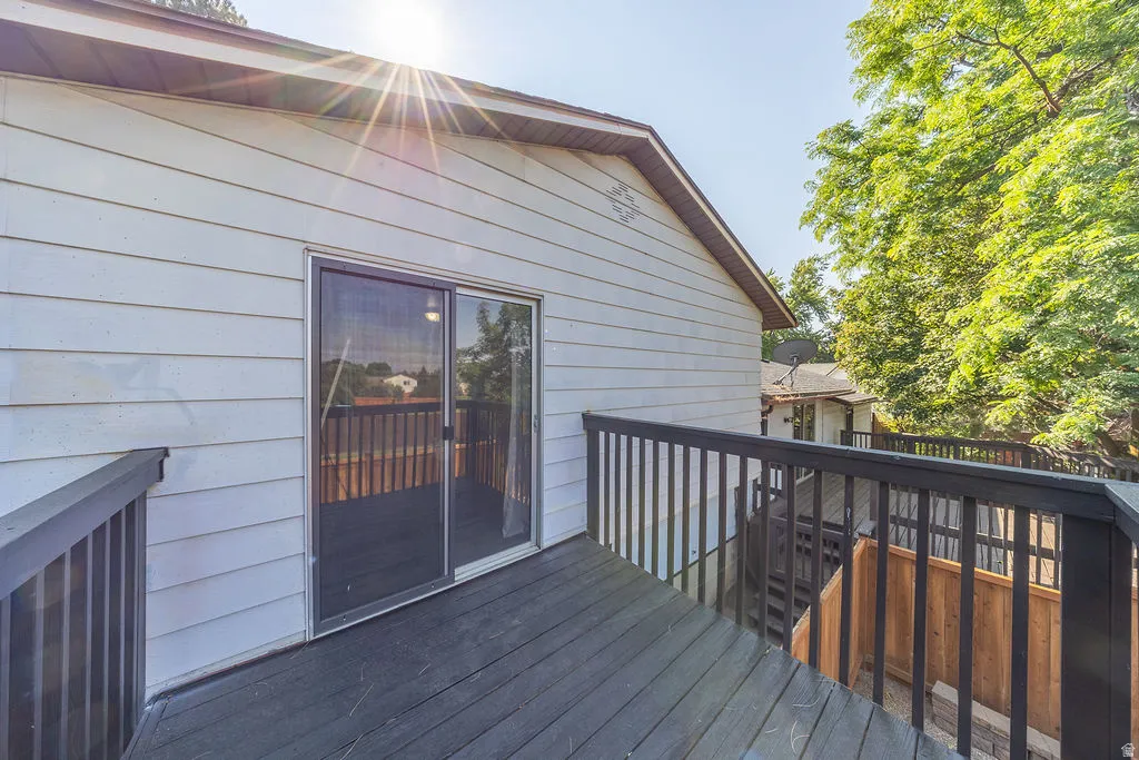 Exterior balcony featuring dark wood-finish decking and railings, white horizontal siding, and a sliding glass door
