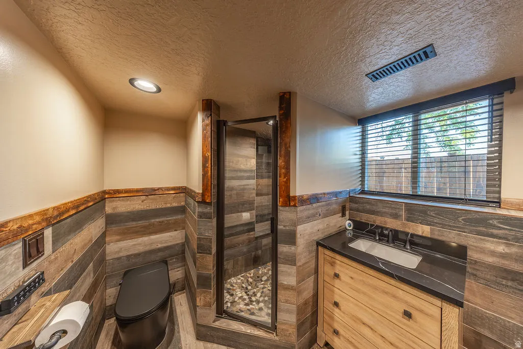 Bathroom featuring plank-style wall and floor tiling, a walk-in shower with a pebble-tiled base, and a vanity with a dark countertop and integrated sink