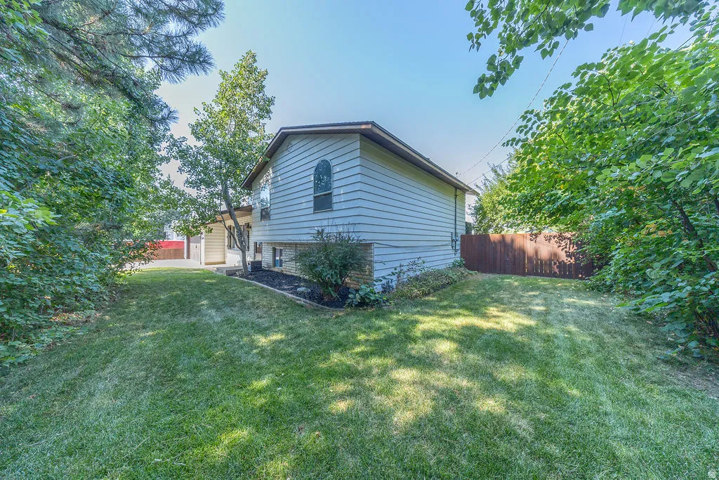 Spacious lawn area with established landscaping, featuring a light-colored siding exterior, an arched window, and a wood privacy fence