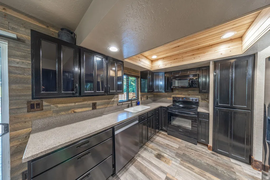 Kitchen featuring a U-shaped countertop layout, black cabinetry with some glass-front uppers, stainless steel appliances, and wood-finish flooring