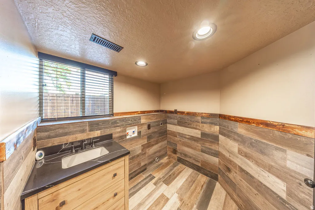 Utility space featuring wood-finish wall and floor tiling, recessed lighting, and a single vanity with dark countertop