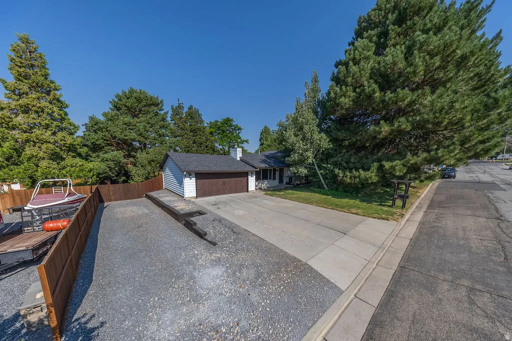 Single-story residence featuring a two-car attached garage with a dark wood-finish door, a graveled area for additional parking, and mature evergreen trees