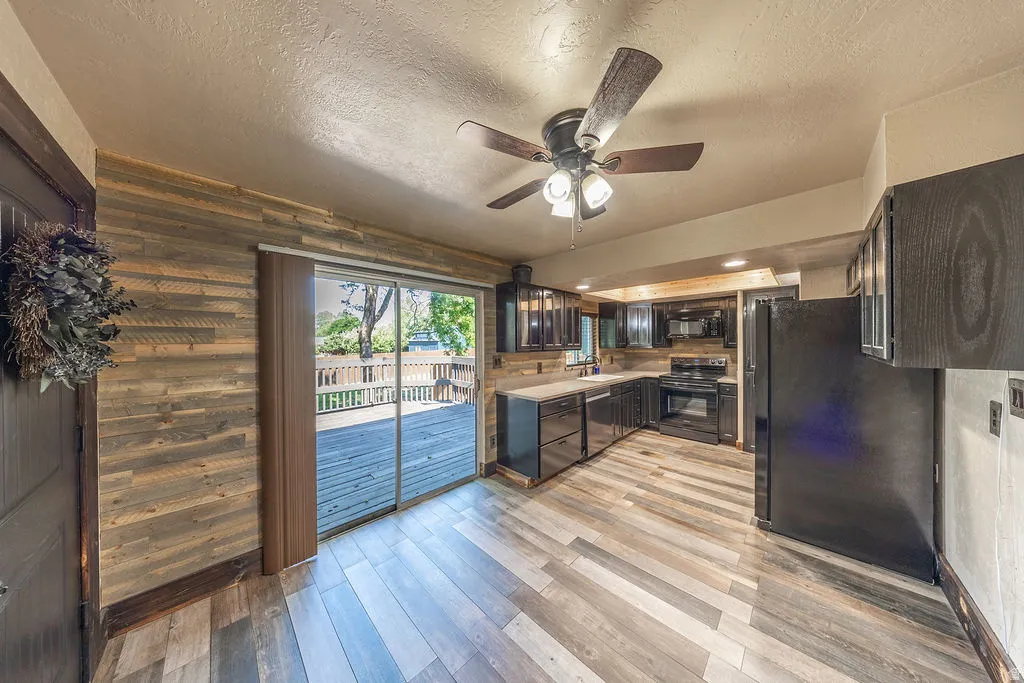 Open-concept living area with wood-finish flooring and a full kitchen featuring black appliances and cabinetry