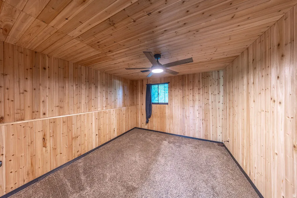 Room featuring extensive wood paneling on walls and ceiling, wall-to-wall carpeting, and a central ceiling fan with integrated lighting
