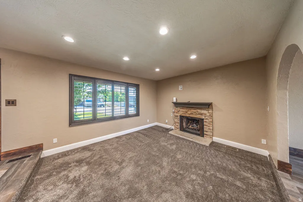 Living area featuring a stone fireplace with a wood mantel, recessed lighting, and a window with plantation shutters