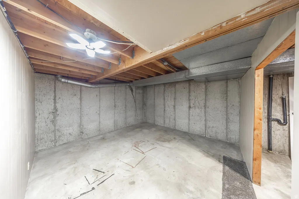 Unfinished basement space featuring exposed concrete walls and flooring, open ceiling joists, and visible ductwork