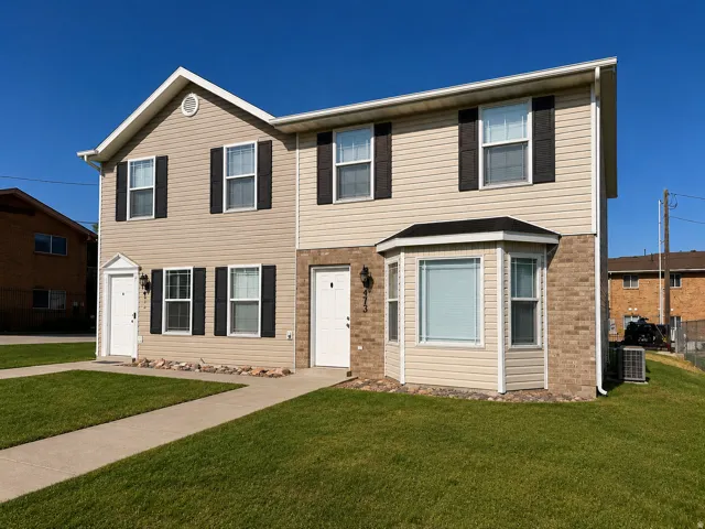 Duplex exterior with light-toned siding, dark shutters, a bay window, and a gabled roofline