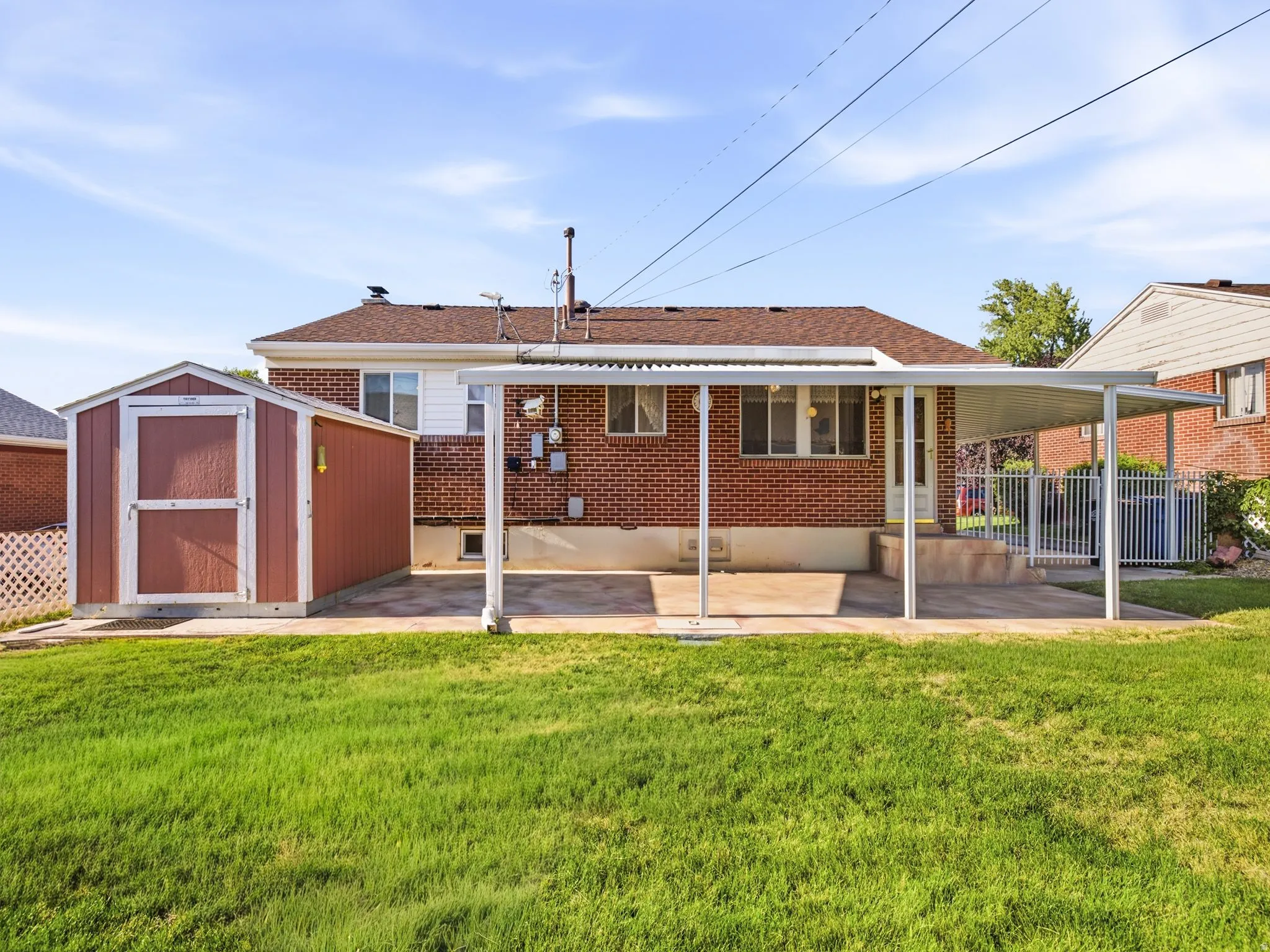 Expansive backyard with a manicured lawn, red brick exterior, covered patio, and a storage shed