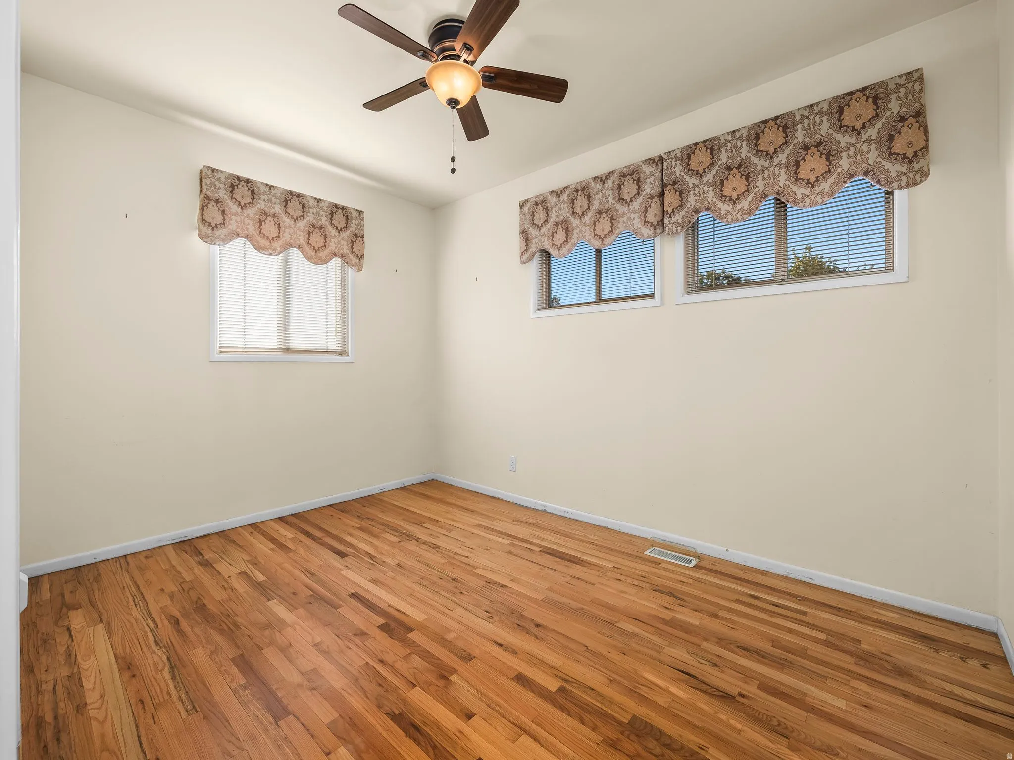 Hardwood flooring with a natural finish, multiple windows, and a ceiling fan with integrated lighting