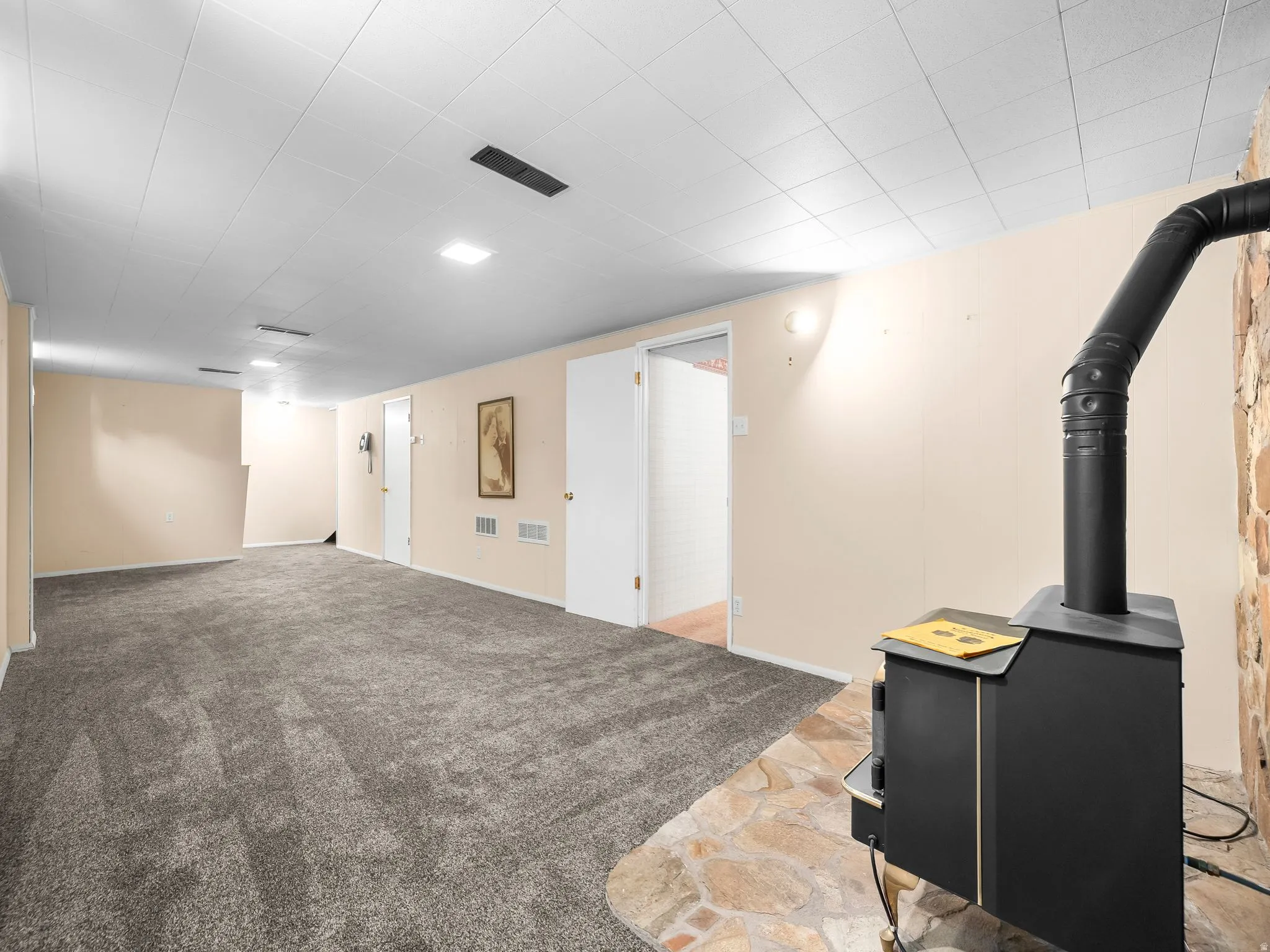 Expansive room featuring gray carpet, a wood-burning stove with a stone surround, and recessed lighting