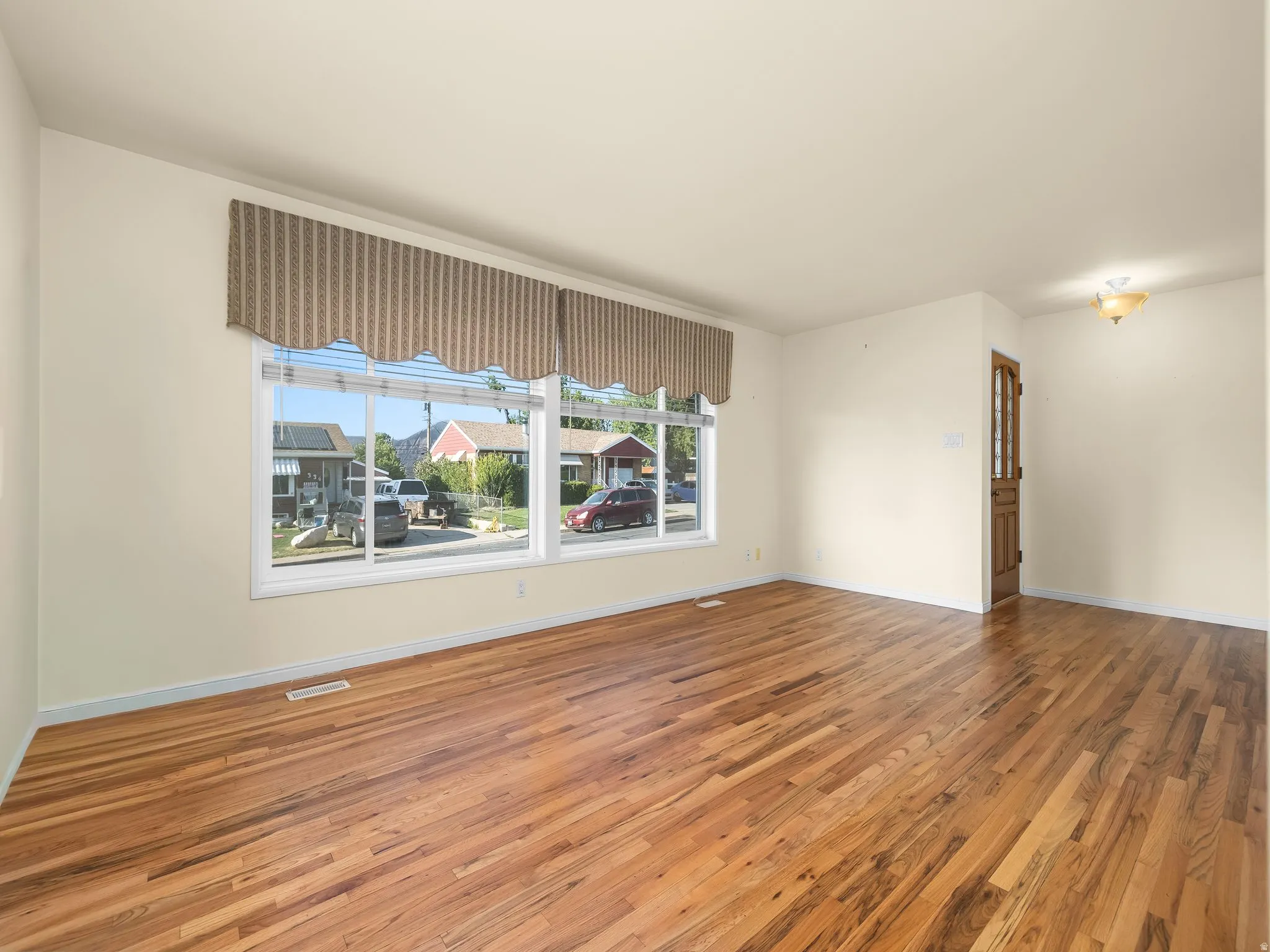 Hardwood flooring, painted walls, large window, wood-paneled door, ceiling light fixture