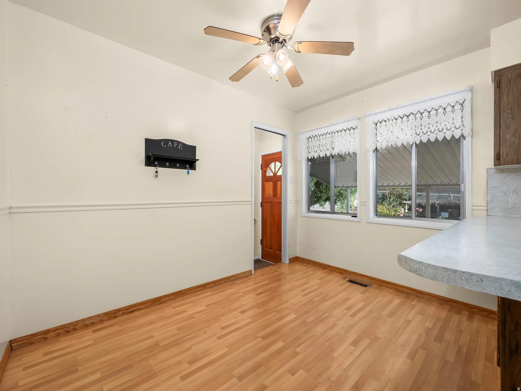 Wood-finish flooring, two large windows, ceiling fan with integrated lighting, two-tone painted walls, and a light-colored countertop