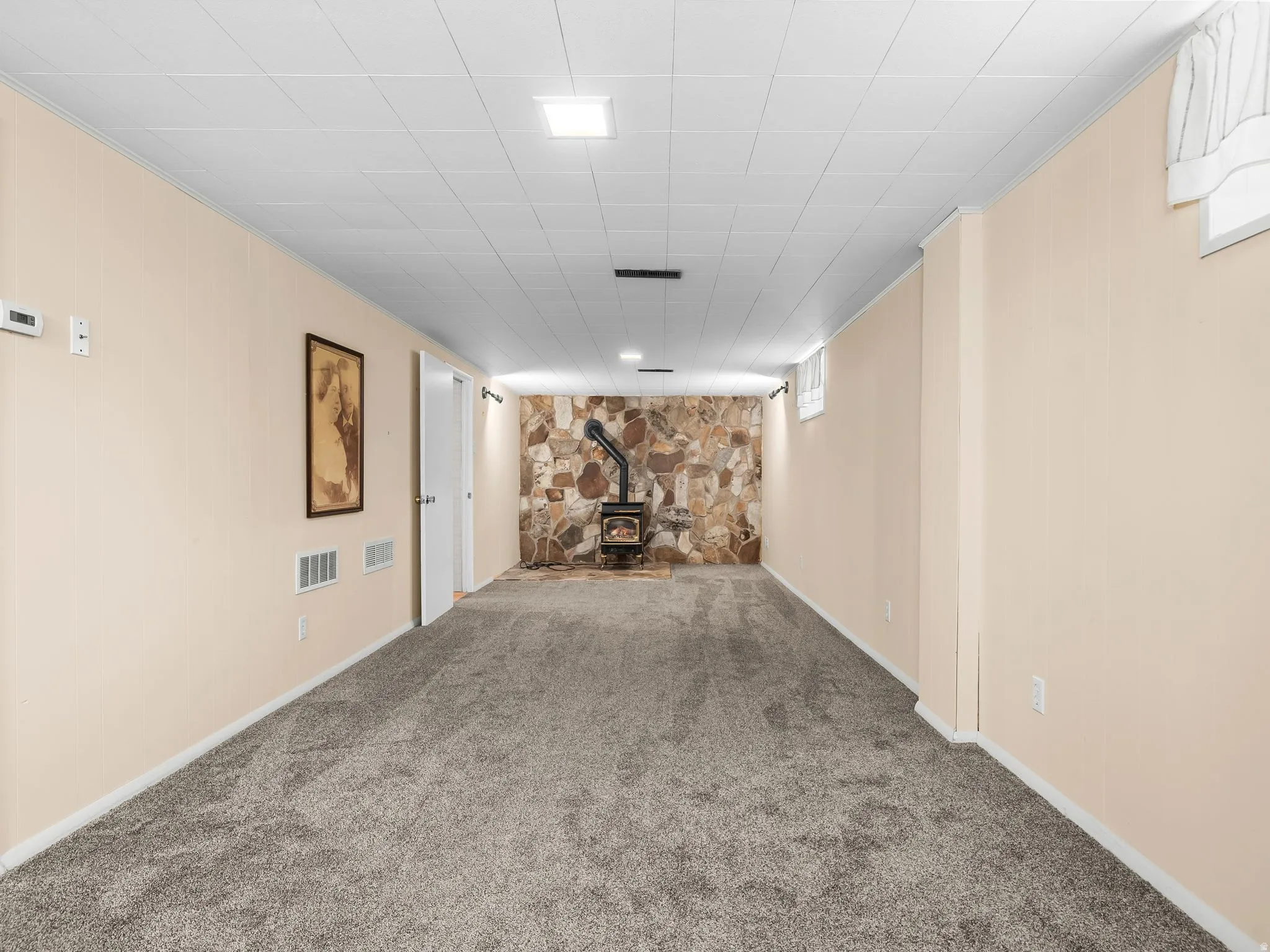 Spacious room featuring carpeting, a natural stone accent wall, and a freestanding wood-burning stove