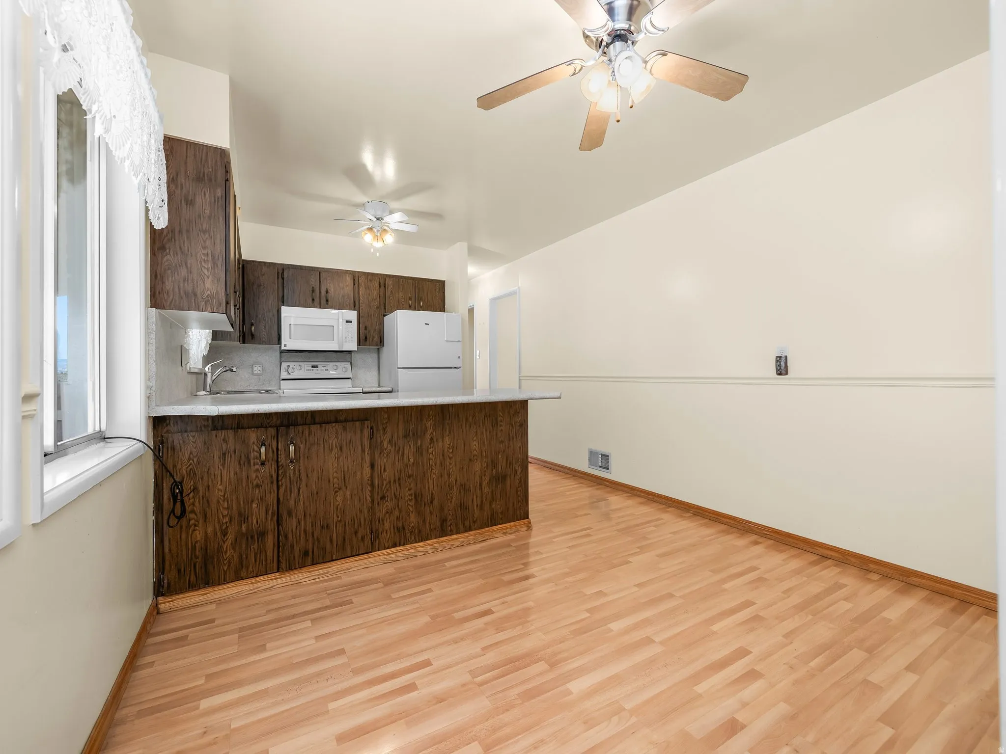 Kitchen featuring wood-finish flooring, dark wood cabinetry, white appliances, a ceiling fan, and a pass-through counter