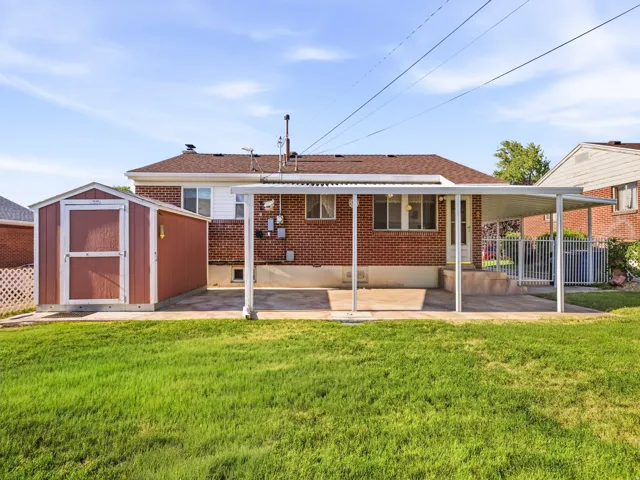 Expansive backyard with a manicured lawn, red brick exterior, covered patio, and a storage shed