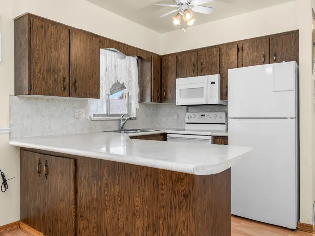 Wood-finish cabinetry and white appliances complement the light-toned countertops, enhanced by a ceiling fan with integrated lighting