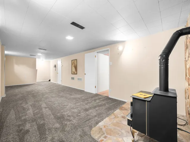 Expansive room featuring gray carpet, a wood-burning stove with a stone surround, and recessed lighting