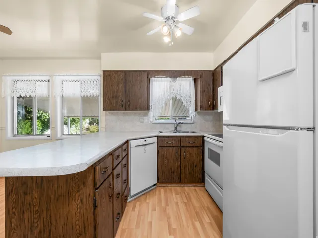 Kitchen with wood-finish cabinetry, light-toned countertops, and integrated white appliances