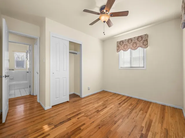 Hardwood flooring, ceiling fan, white bi-fold closet doors, window with blinds, and white bathroom tile flooring