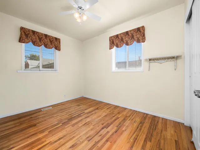 Wood-finish flooring, white ceiling fan with integrated lighting, and two windows with blinds