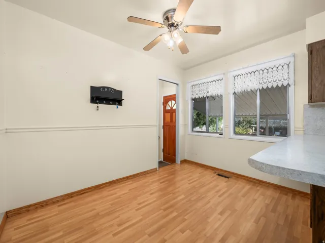 Wood-finish flooring, two large windows, ceiling fan with integrated lighting, two-tone painted walls, and a light-colored countertop