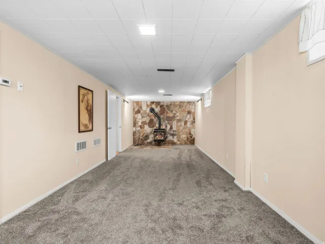 Spacious room featuring carpeting, a natural stone accent wall, and a freestanding wood-burning stove
