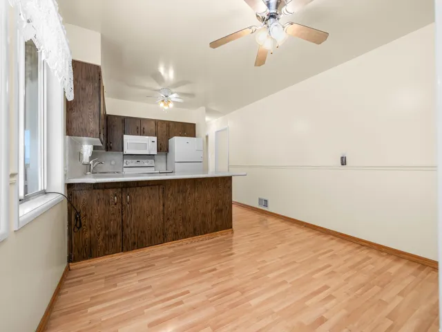 Kitchen featuring wood-finish flooring, dark wood cabinetry, white appliances, a ceiling fan, and a pass-through counter