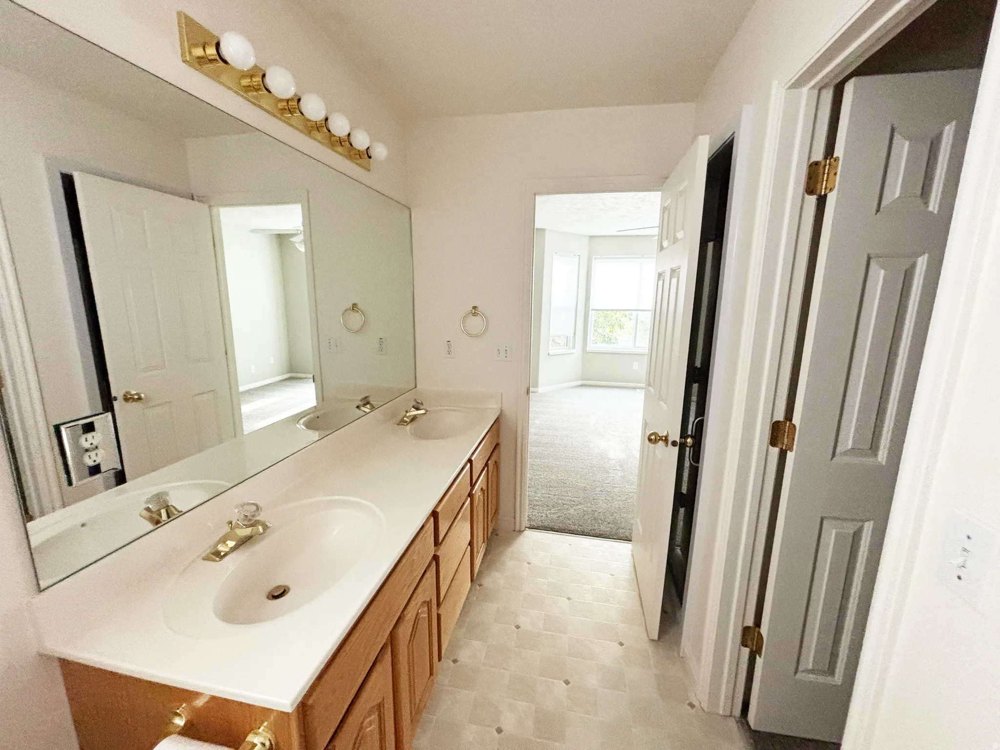Dual vanity with integrated sinks, expansive wall-mounted mirror, brass-finish light fixture, and wood-finish cabinetry