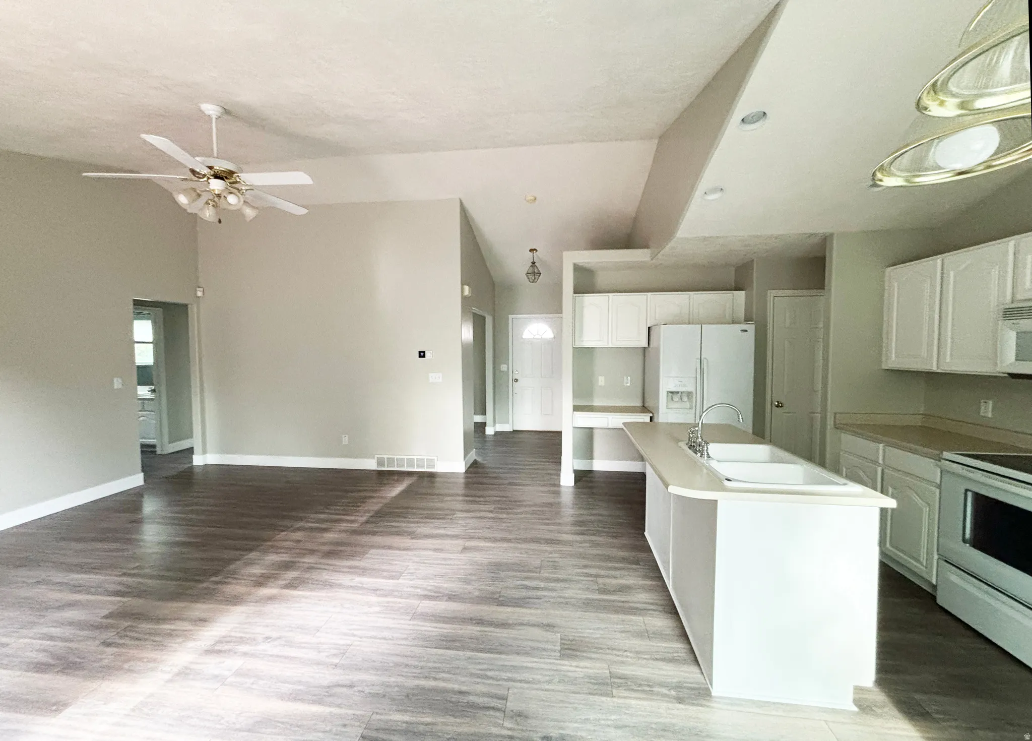 Open-concept kitchen and living area featuring wood-finish flooring throughout, white cabinetry with stainless steel appliances, a large center island with white base, and a ceiling fan with integrated lighting