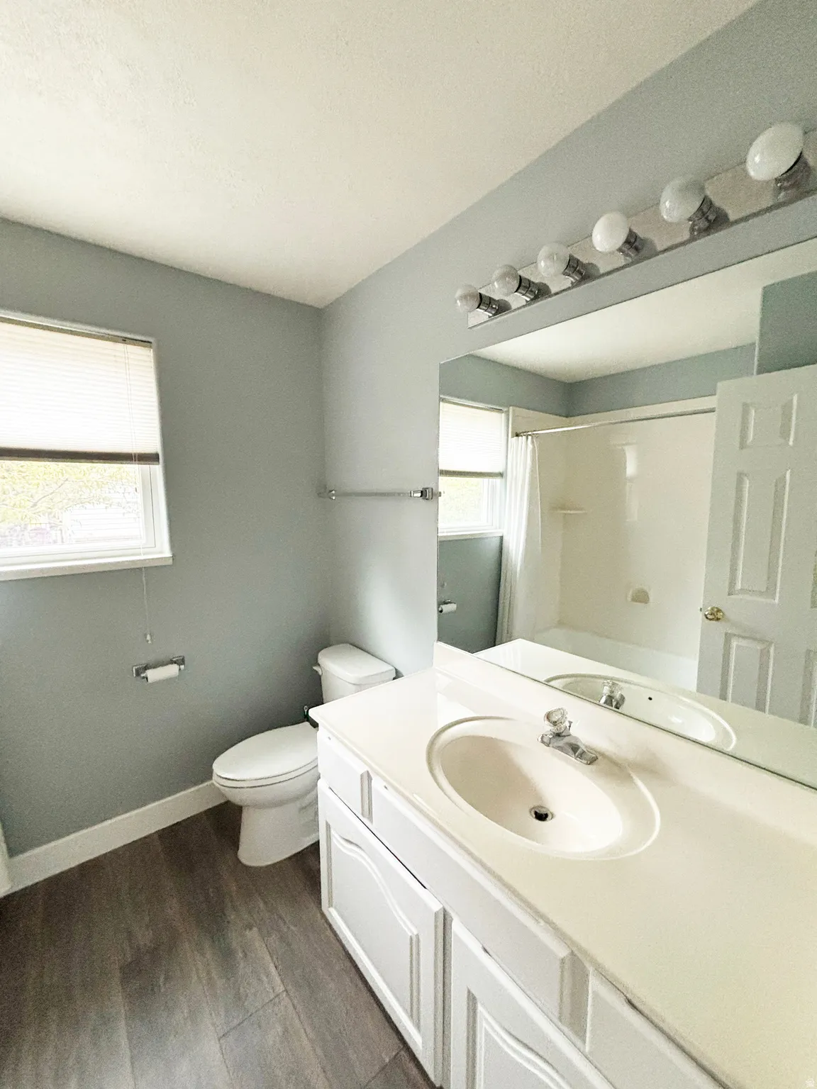 Bathroom featuring a white vanity with integrated sink, wood-finish flooring, a toilet, a full-width mirror, and a bathtub with shower