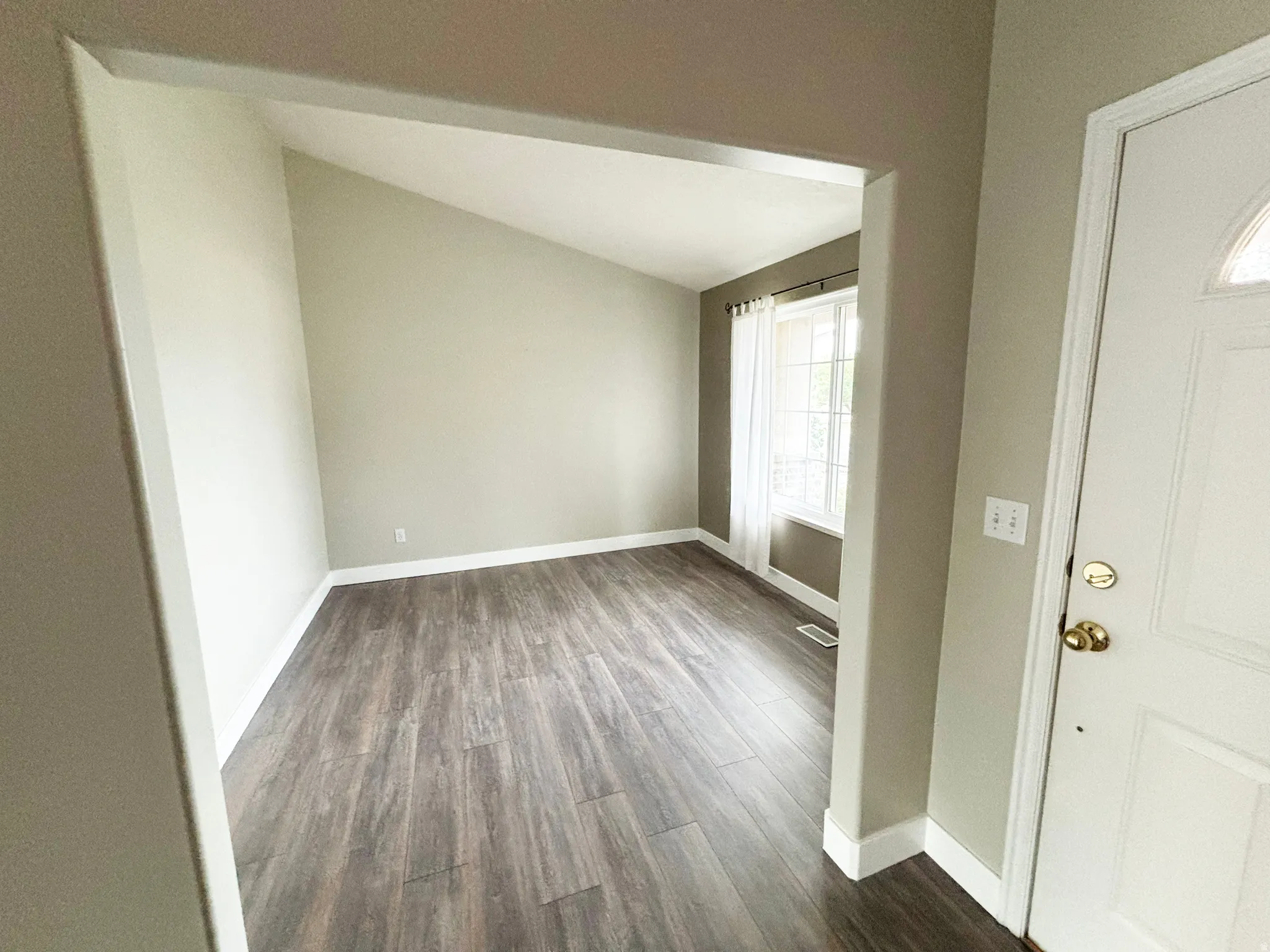 Bright corner room featuring wood-finish flooring, abundant natural light from dual windows, and clean white architectural trim throughout