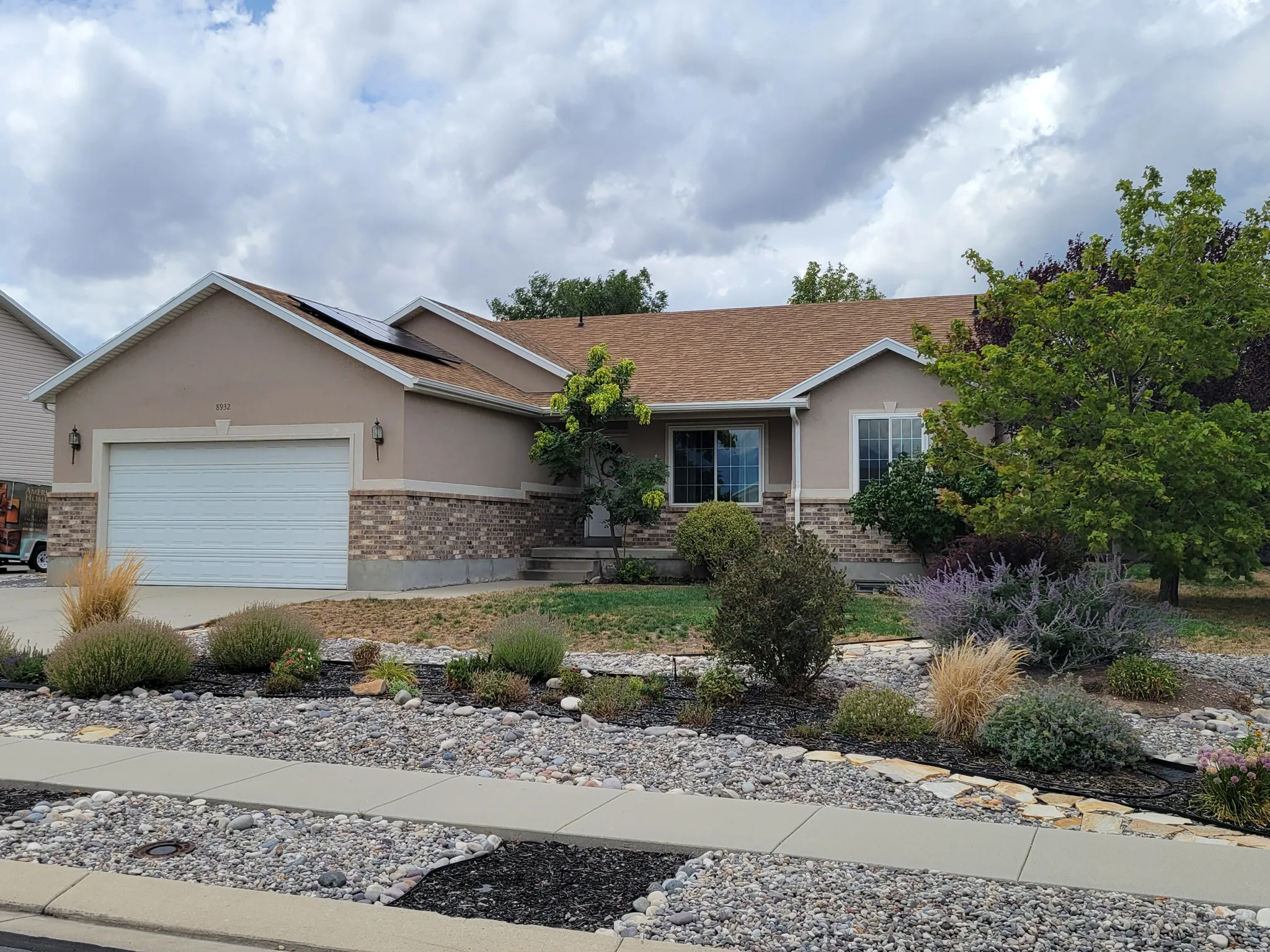 Stucco exterior with stone accent, attached garage, and mature landscaping