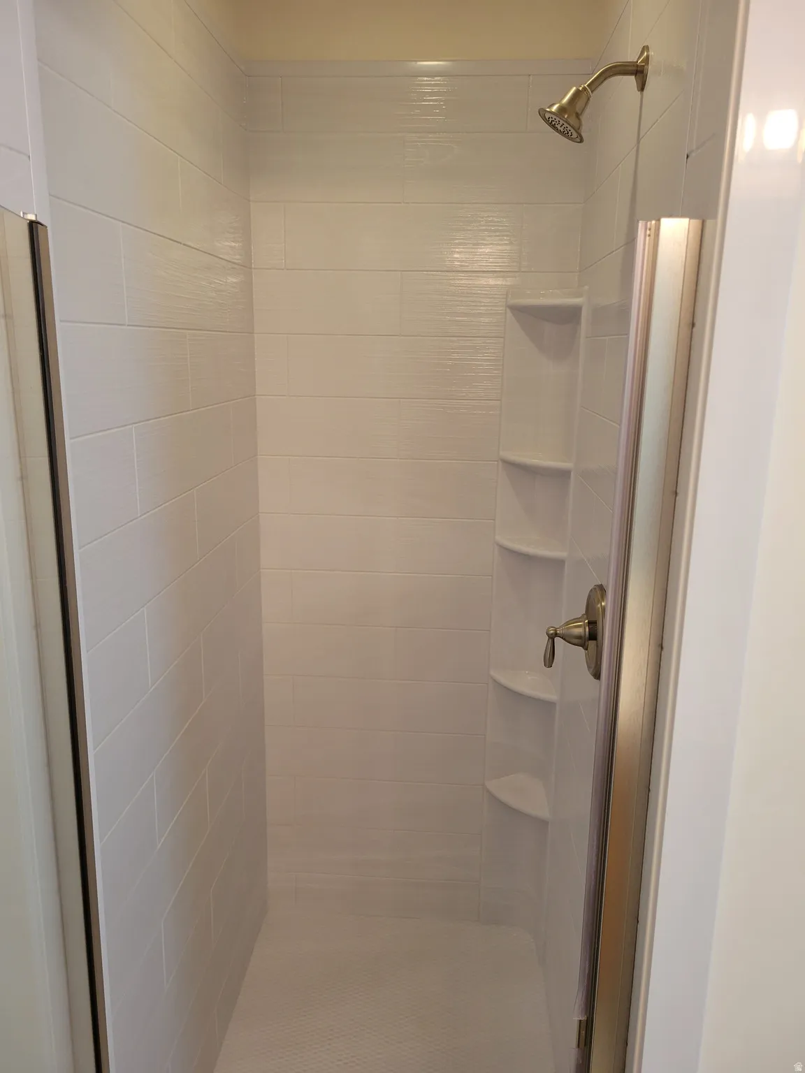 Walk-in shower with horizontal white tile, built-in corner shelving, and a bronze-finish showerhead