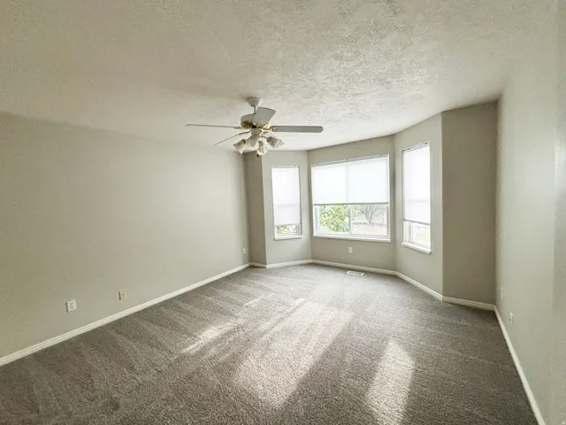 Expansive room with neutral carpeting, a ceiling fan, and multiple windows with blinds