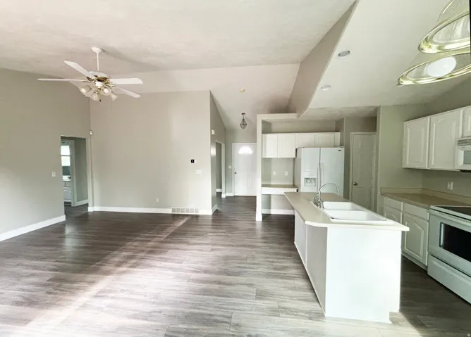 Open-concept kitchen and living area featuring wood-finish flooring throughout, white cabinetry with stainless steel appliances, a large center island with white base, and a ceiling fan with integrated lighting