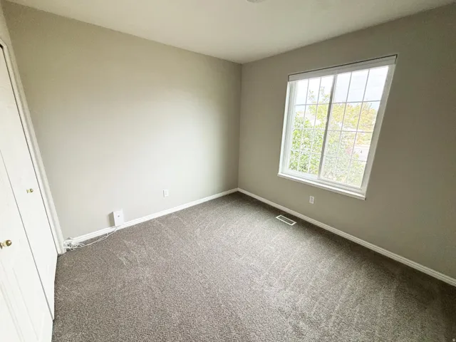 Bright secondary bedroom featuring neutral wall finishes, expansive carpeting, and abundant natural light from a large double-hung window with gridded panes