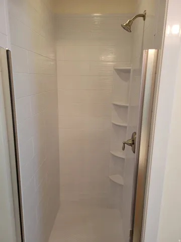 Walk-in shower with horizontal white tile, built-in corner shelving, and a bronze-finish showerhead