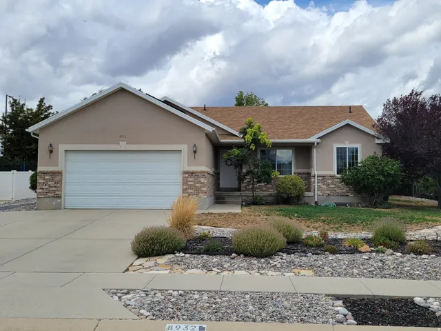 Stucco and stone veneer exterior with a concrete driveway, a wood-finish garage door, and a shingle roof