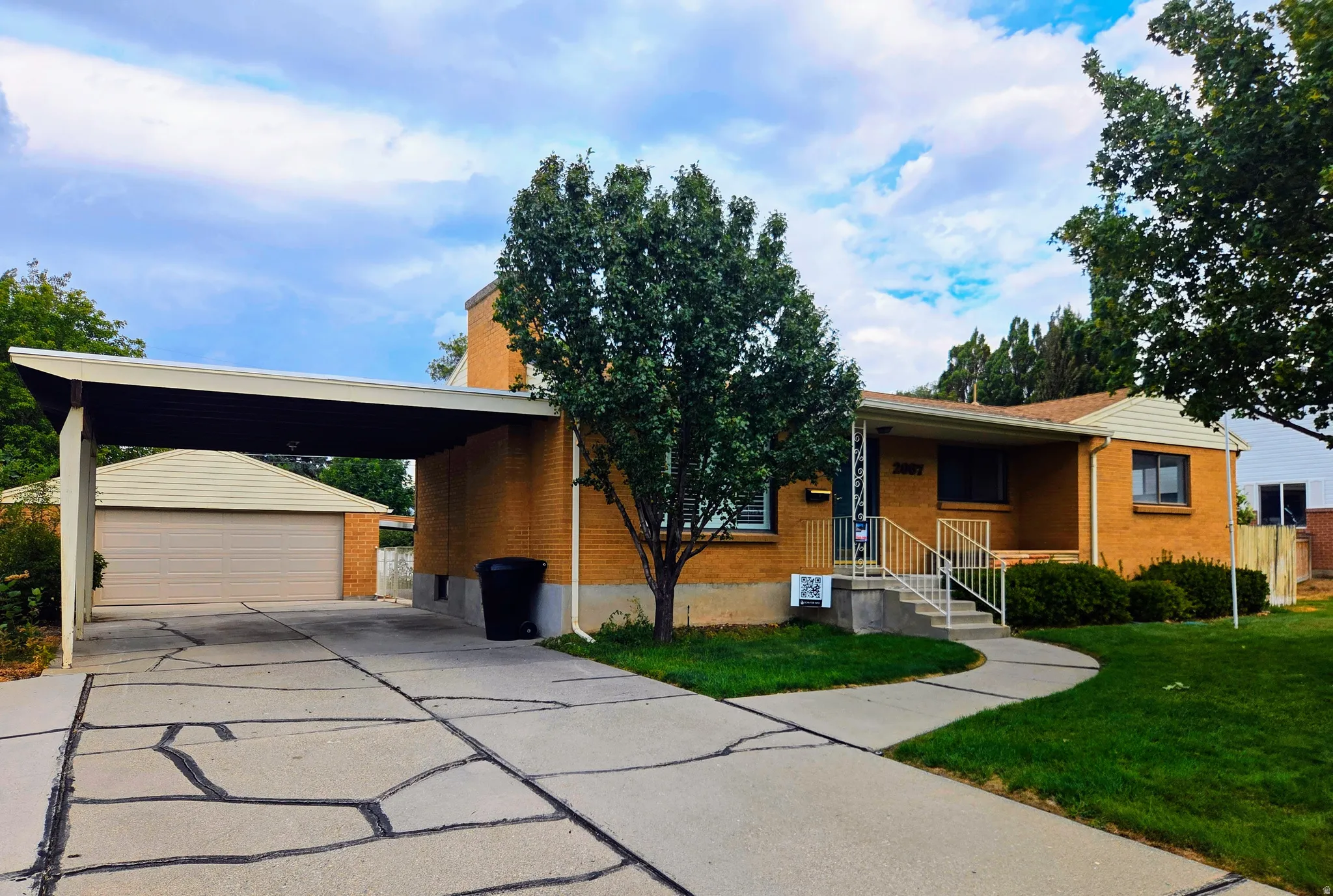 Brick exterior with a covered carport, attached garage, concrete driveway, and front walk-up with handrails
